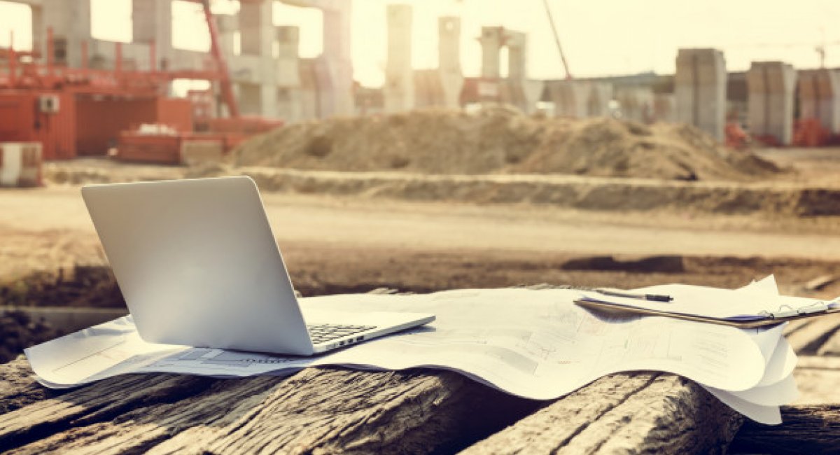 Building rapport laptop on blueprints in foreground of construction site