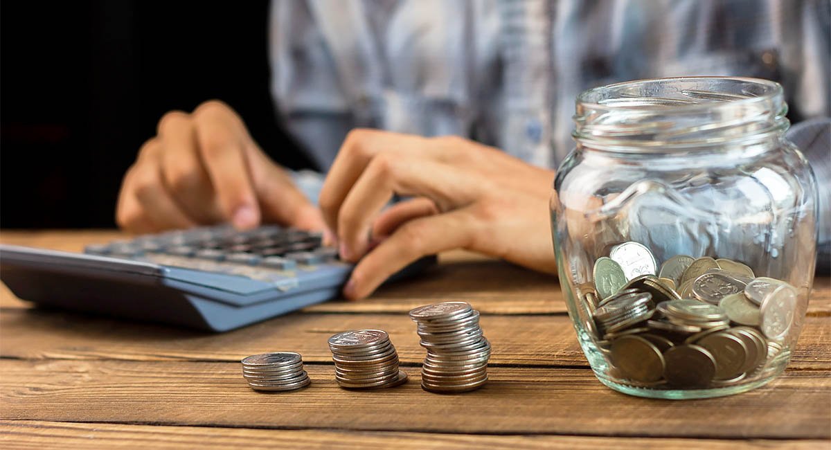 How much can I save? Man's hands, calculator, coins in a jar