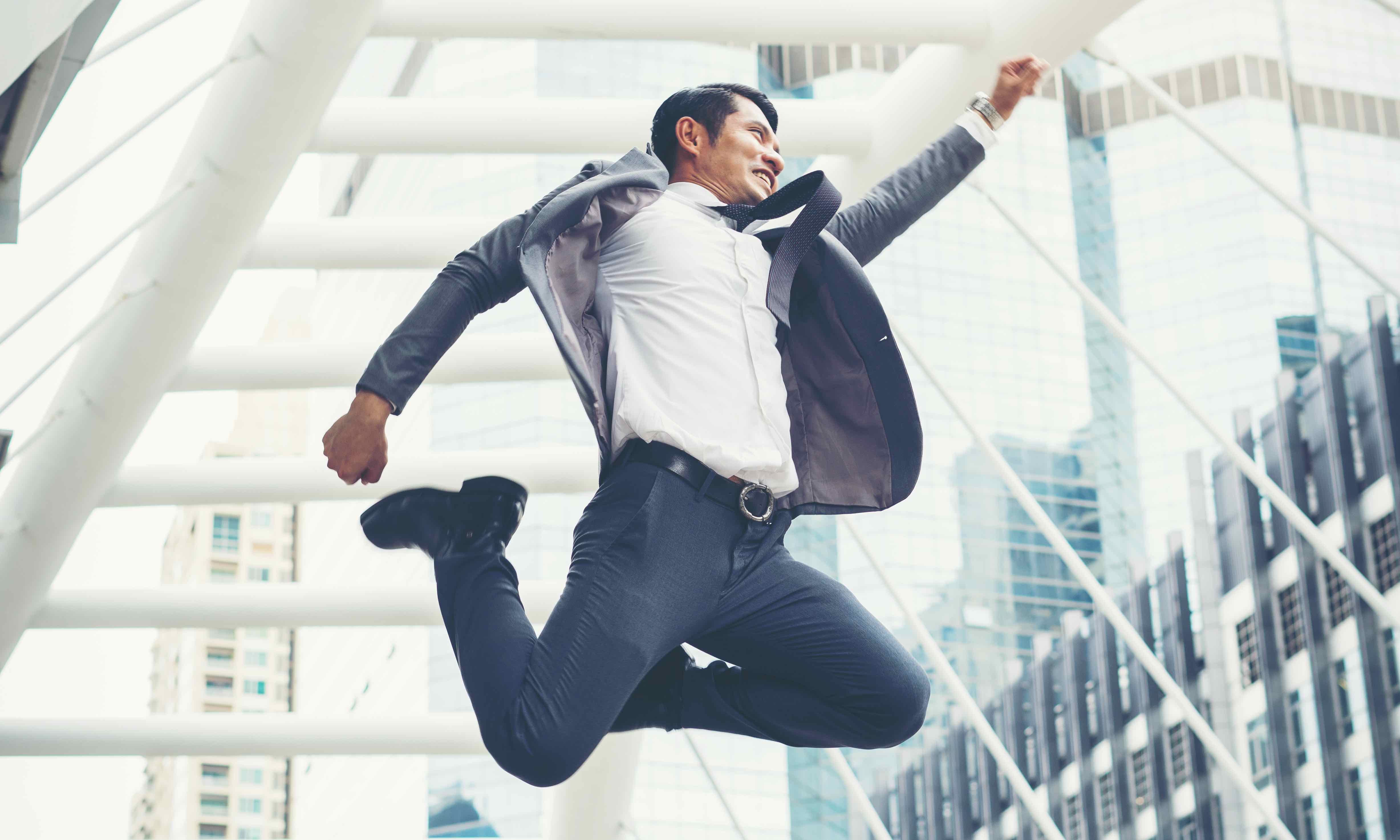 man in business suit jumping for joy by office buildings