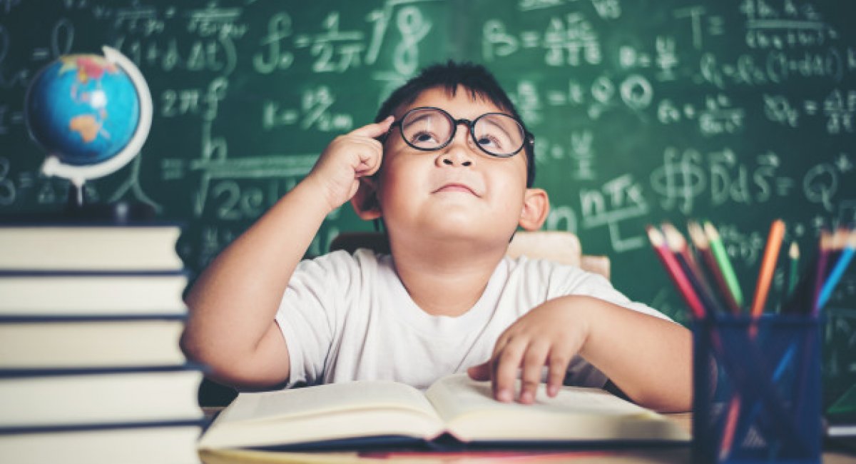 Boy at a desk in school with a stack of books