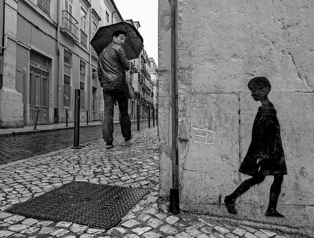 man walking down cobblestone street looking back at silhouette figure of girl on wall