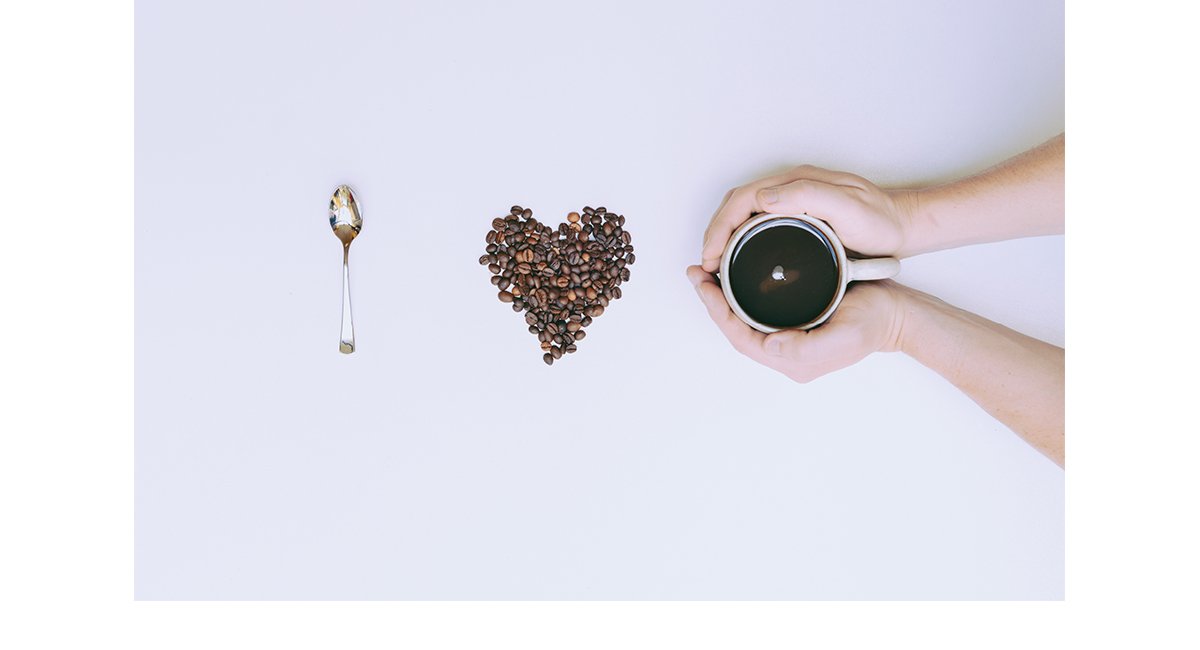 Spoon, heart made with coffee beans, and hands holding coffee cup = "I love coffee"