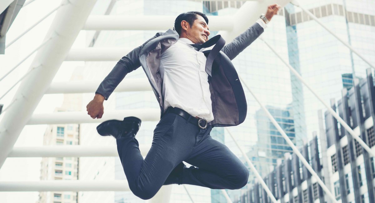 man in business suit jumping with excitement in middle of city street
